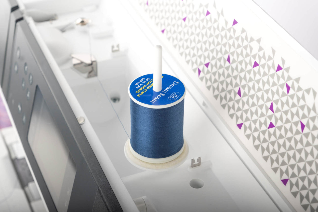 a blue spool of dream seam cotton thread on a sewing machine pin