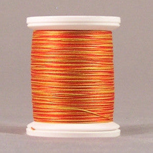 Orange and yellow variegated thread wound on white plastic spool against neutral background