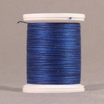 Blue thread spool with white plastic ends, showing tightly wound hyacinth blue thread on a neutral background