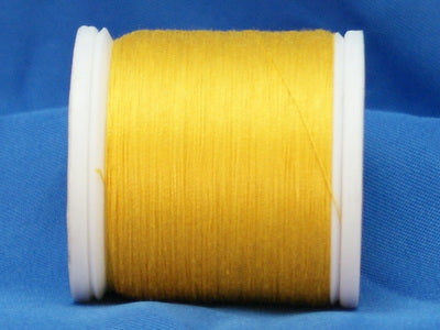 Yellow thread wound on white plastic spool against blue fabric background