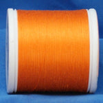 Orange thread wound on white plastic spool against blue fabric background