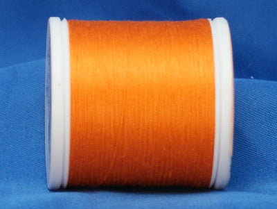 Orange thread wound on white plastic spool against blue fabric background