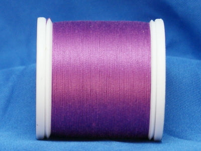 Magenta thread wound on white plastic spool against blue fabric background