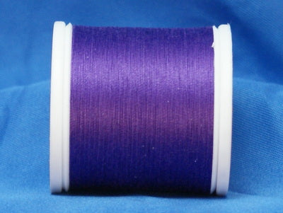 Purple thread wound on white plastic spool against blue fabric background