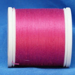 Bright fuchsia thread wound on white plastic spool against blue fabric background