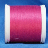 Bright fuchsia thread wound on white plastic spool against blue fabric background