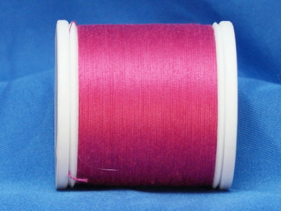 Bright fuchsia thread wound on white plastic spool against blue fabric background