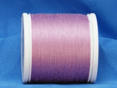 Pink gradient thread spool on white plastic bobbin against blue fabric background