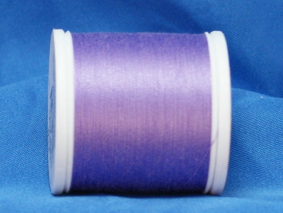 Lavender purple thread on white plastic spool against blue fabric background