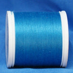 Turquoise thread wound on white plastic spool against blue fabric background