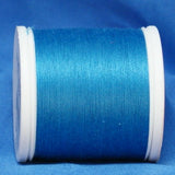 Turquoise thread wound on white plastic spool against blue fabric background