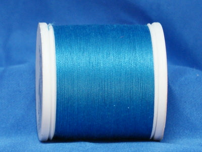 Turquoise thread wound on white plastic spool against blue fabric background