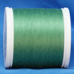 Fern green thread wound on white plastic spool against blue fabric background