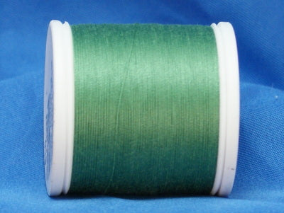 Fern green thread wound on white plastic spool against blue fabric background