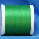 Green thread wound on white plastic spool against blue fabric background