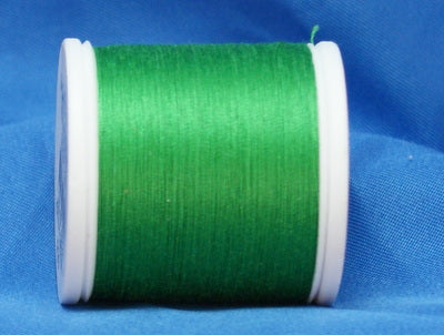 Green thread wound on white plastic spool against blue fabric background