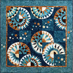 Batik quilt kit featuring curved spiral designs in teal, navy, rust orange and cream colors with geometric triangular patterns and circular motifs