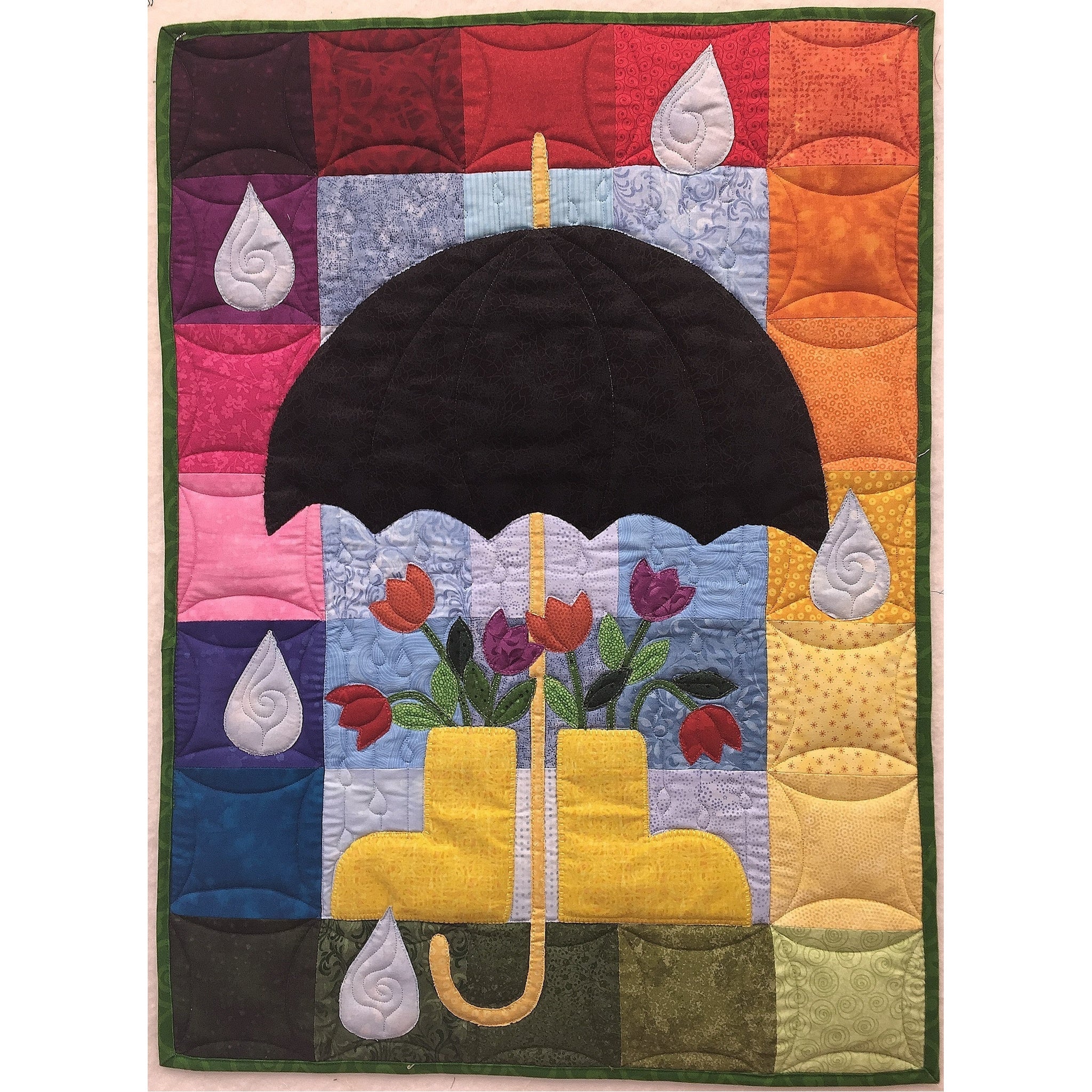 Colorful quilted wall hanging featuring a black umbrella with spring flowers and raindrops on a rainbow gradient background.