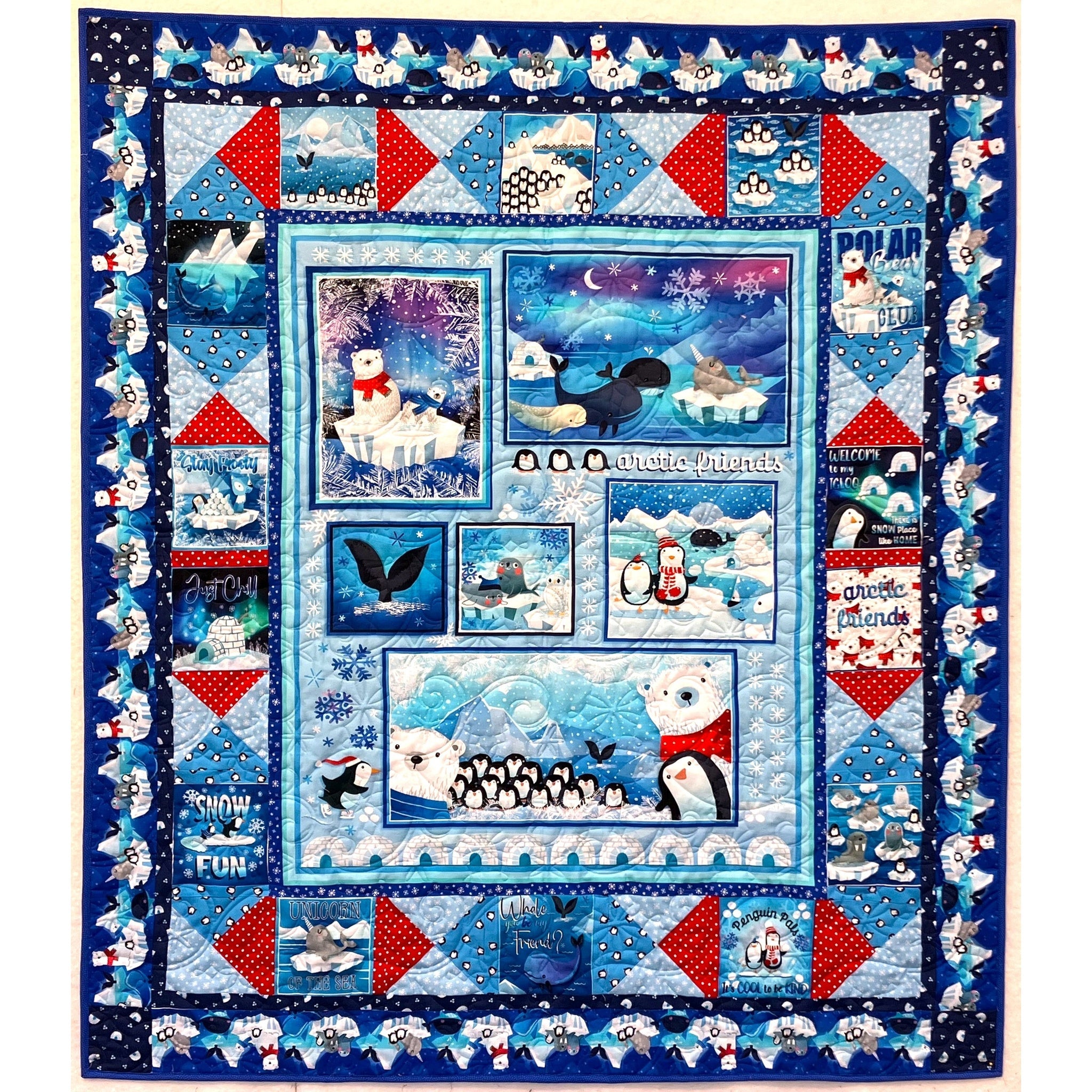 A winter-themed quilt featuring Arctic animals like polar bears, penguins, and whales in blue, white, and red fabrics with snowflake patterns and geometric borders.