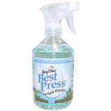 A clear spray bottle with white trigger nozzle containing light blue-green liquid, labeled "Mary Ellen's Best Press" with Caribbean beach imagery on the label.