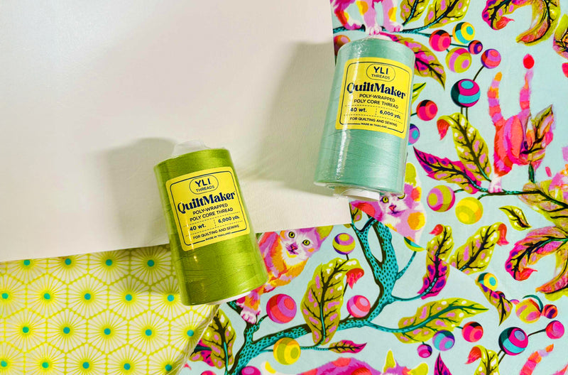 two cones of YLI Threads quiltmaker on colorful fabrics