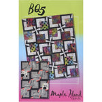 Colorful quilt pattern featuring geometric blocks with vibrant florals and contrasting black sashing, displayed on gradient green-to-pink background.