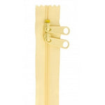 Pale yellow zipper with two cream-colored pull tabs on a light yellow tape background.