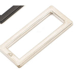 Nickel-plated flat rectangular metal ring with rounded corners and embossed logo, shown alongside a dark metal piece on white background.