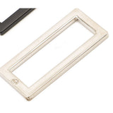 Nickel-plated flat rectangular metal ring with rounded corners and embossed logo, shown alongside a dark metal piece on white background.