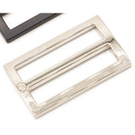 Nickel-plated rectangular metal slider hardware with wide mouth opening, shown alongside black hardware pieces on white background.
