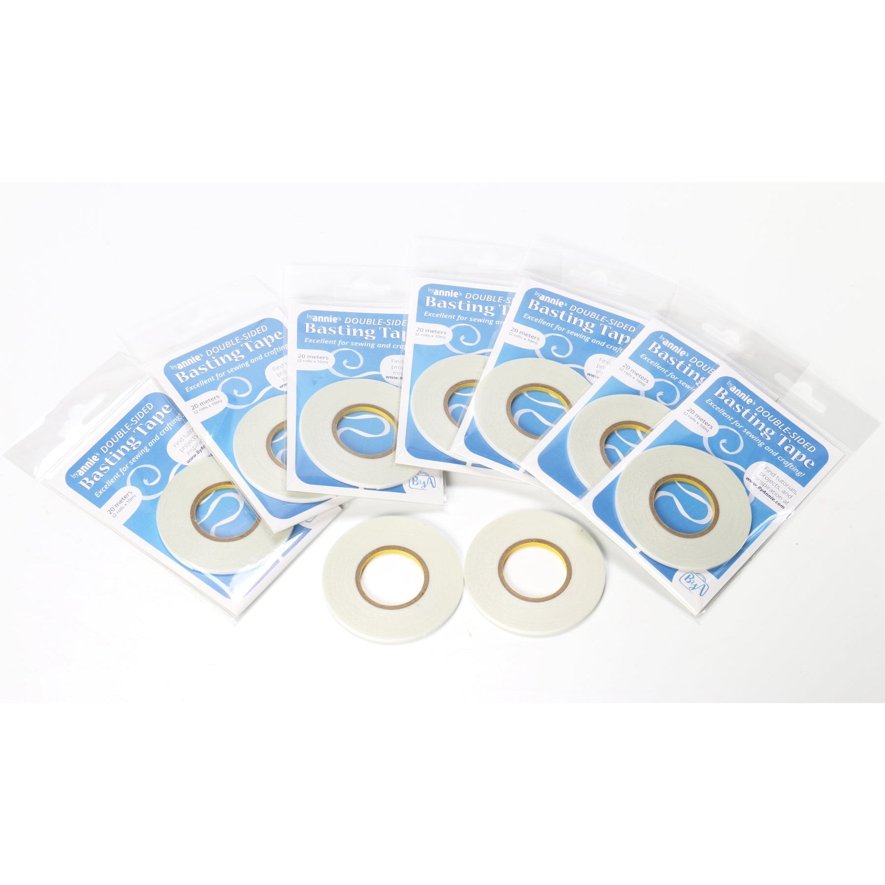 Several packages of ByAnnie's white double-sided basting tape in blue packaging, with two loose tape rolls displayed in front.