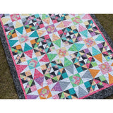 Colorful triangle-pattern quilt with vibrant fabrics in pink, teal, orange, and purple with white accents and dark floral border.
