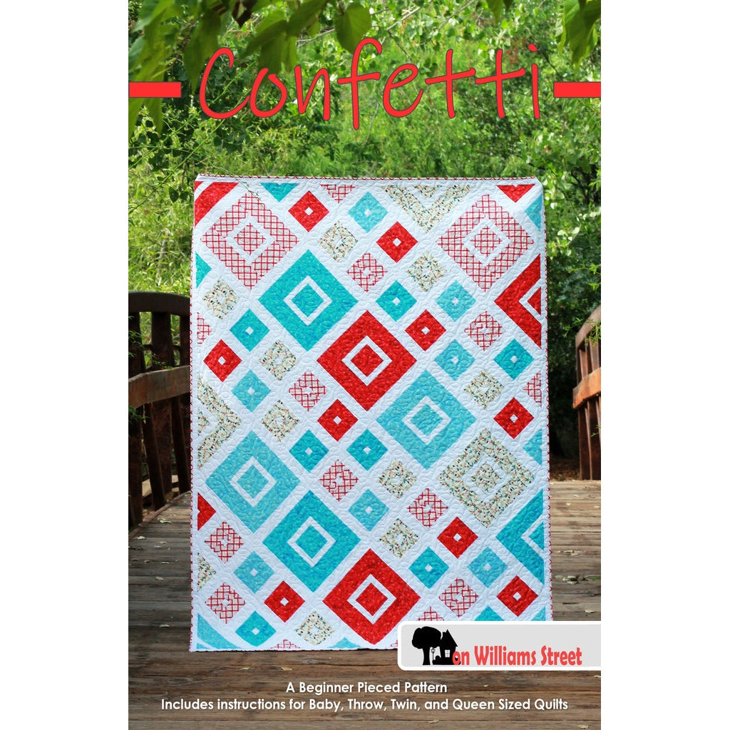 A colorful quilt pattern featuring diamond shapes in red, turquoise, and white arranged in a geometric design on a wooden deck.