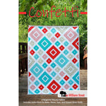 A colorful quilt pattern featuring diamond shapes in red, turquoise, and white arranged in a geometric design on a wooden deck.