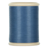 Gray blue hand quilting thread wound on white plastic spool with cream-colored ends