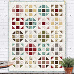 Barnyard Happy Farm quilt kit featuring geometric blocks in cream, red, yellow, teal, and brown with farm-themed prints displayed against white brick wall