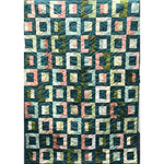 A quilted blanket featuring interlocking square blocks in teal, coral, cream, and olive green fabrics with curved piecing that creates dimensional depth.