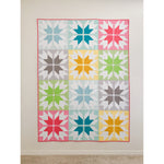 Colorful star pattern quilt with 12 blocks in pink, teal, yellow, green, and gray displayed on a white wall with coral binding.