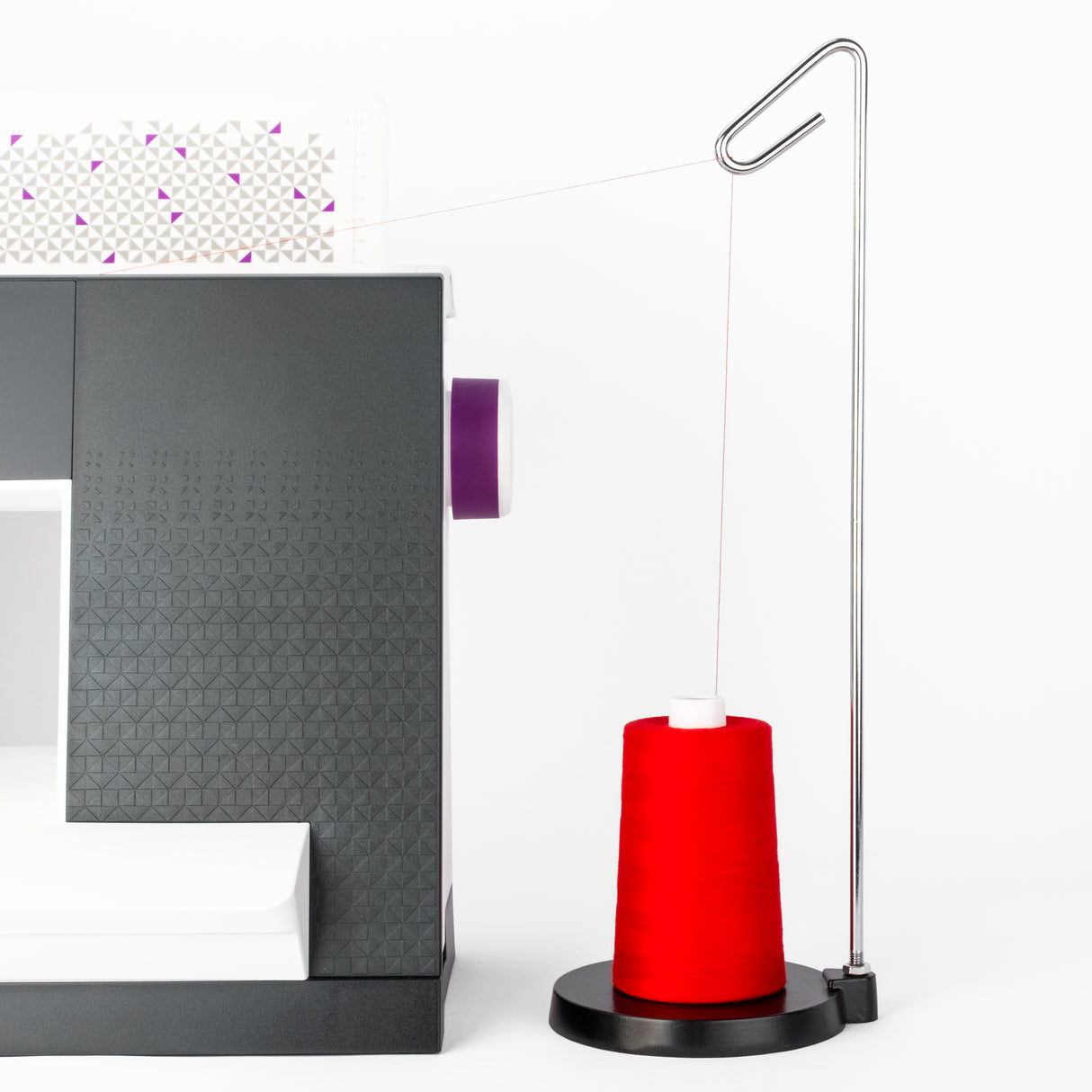 red cone of QuiltMaker polyester thread on a metal thread stand next to a sewing machine