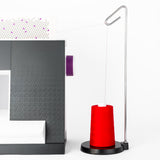 red cone of QuiltMaker polyester thread on a metal thread stand next to a sewing machine