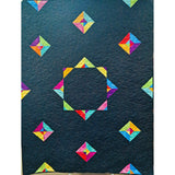 A dark teal quilt featuring colorful geometric pinwheel blocks arranged around a central octagonal design with decorative spiral quilting.