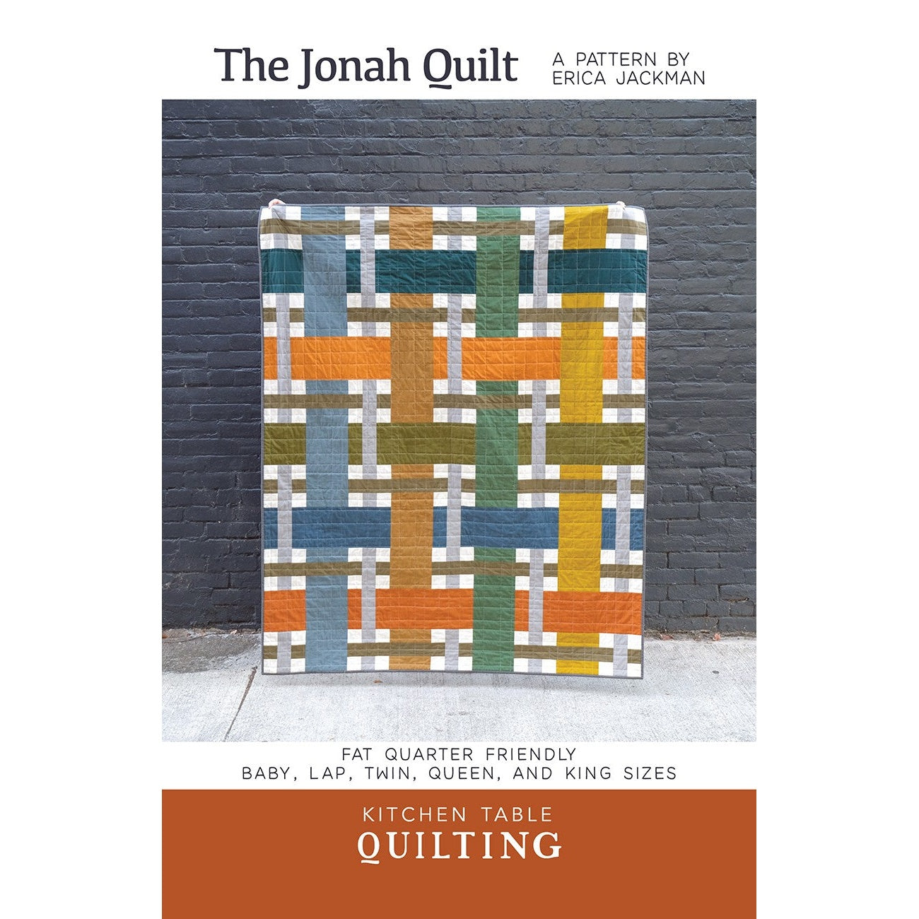 A colorful geometric quilt pattern featuring interlocking blocks in blues, oranges, greens, and yellows displayed against a dark brick wall.