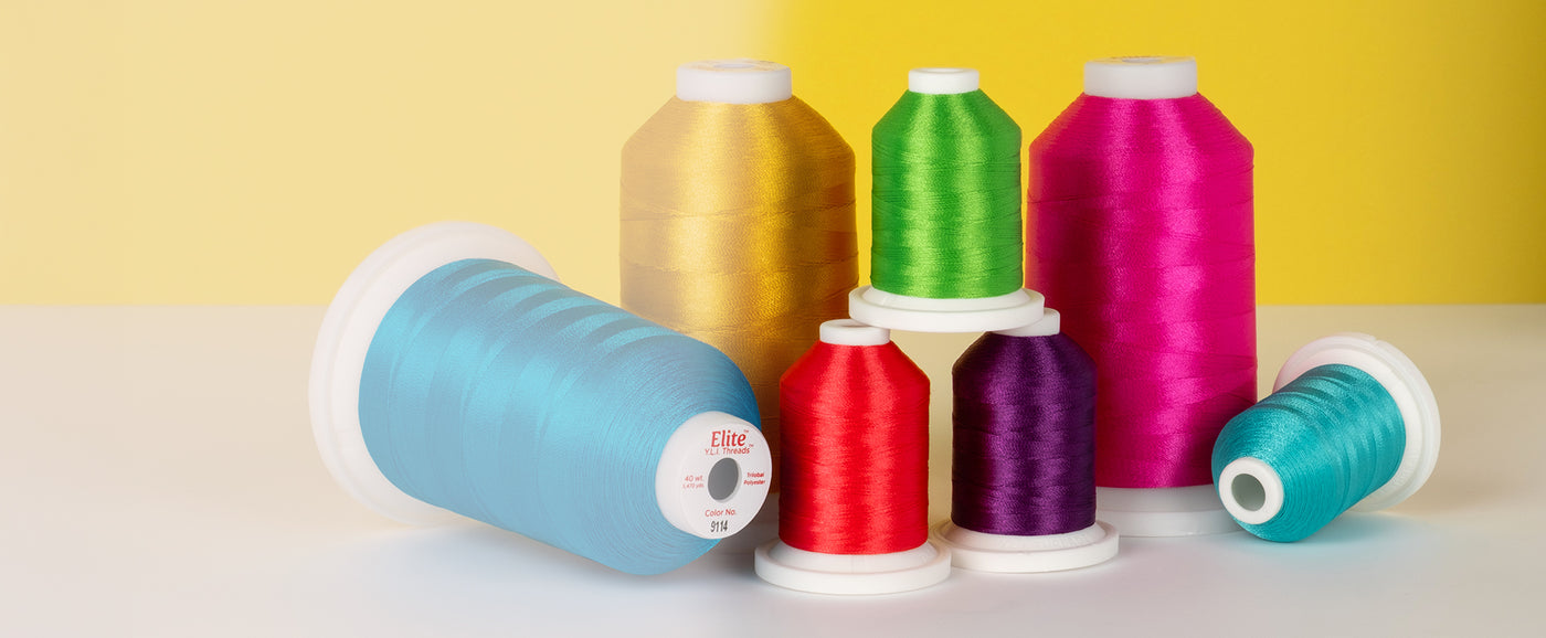 Cones of Elite trilobal polyester quilting thread in front of a yellow background