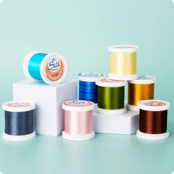group of colorful yli silk 100 wt spools with green background
